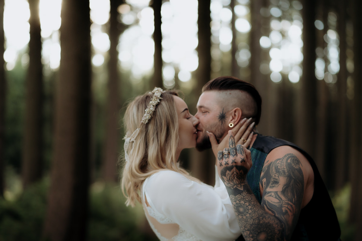 Ein tätowiertes Hochzeitspaar zeigt Mittelfinger im Wald bei After Wedding Shooting Dresden
